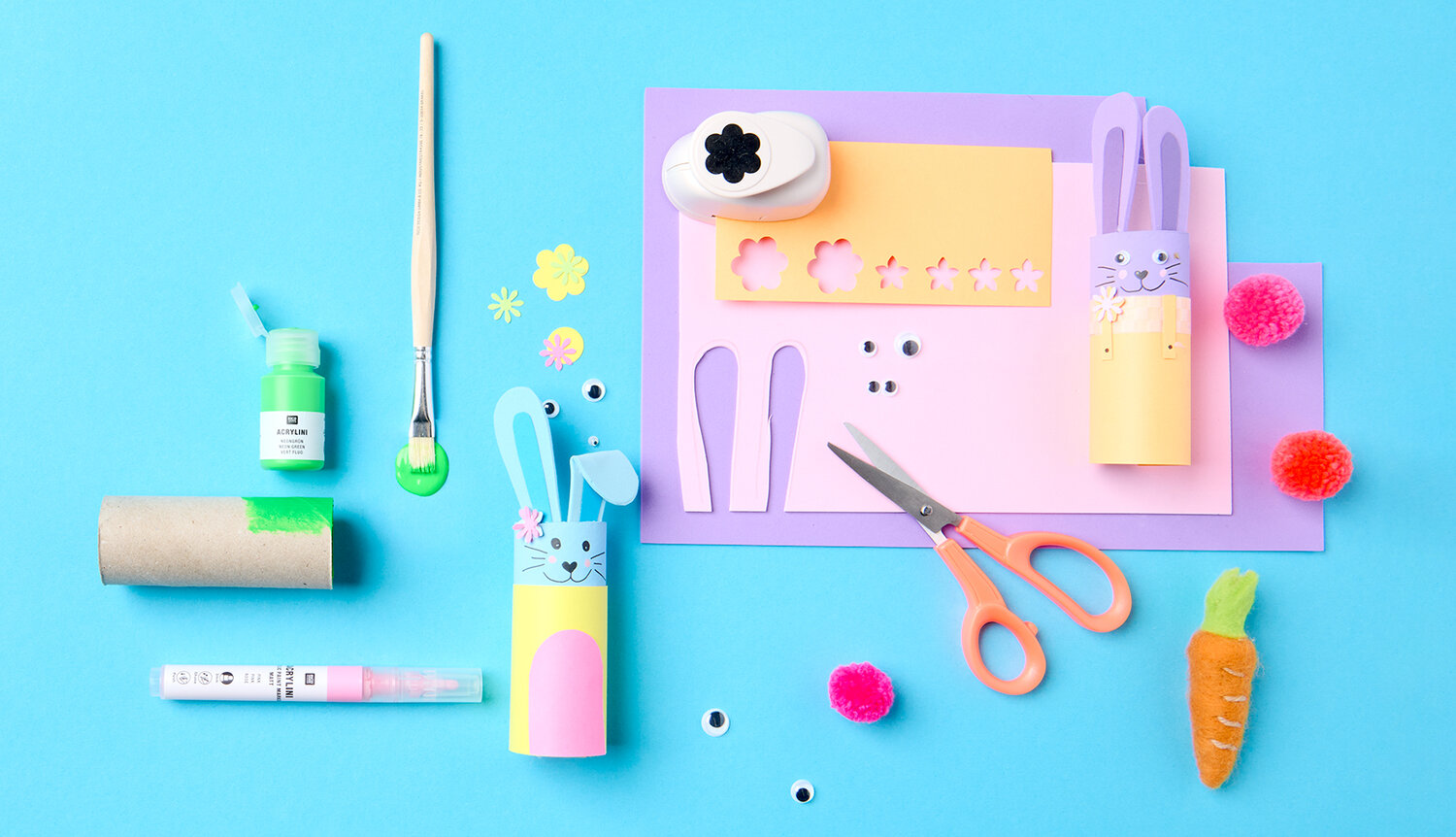 Bastelanleitung Osterhasen aus Klopapierrollen: Materialien auf blauem Hintergrund, inkl. Schere, Pinsel, Papier und Farben.