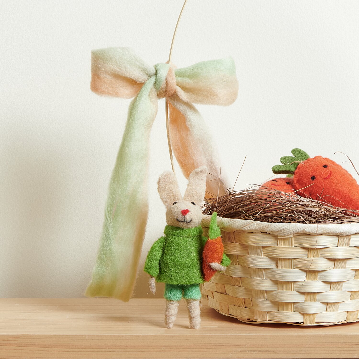 Bambus Korb mit Henkel Weiß, gefüllt mit Filz-Möhren, daneben ein Filz-Hase mit Pulli und Möhre.