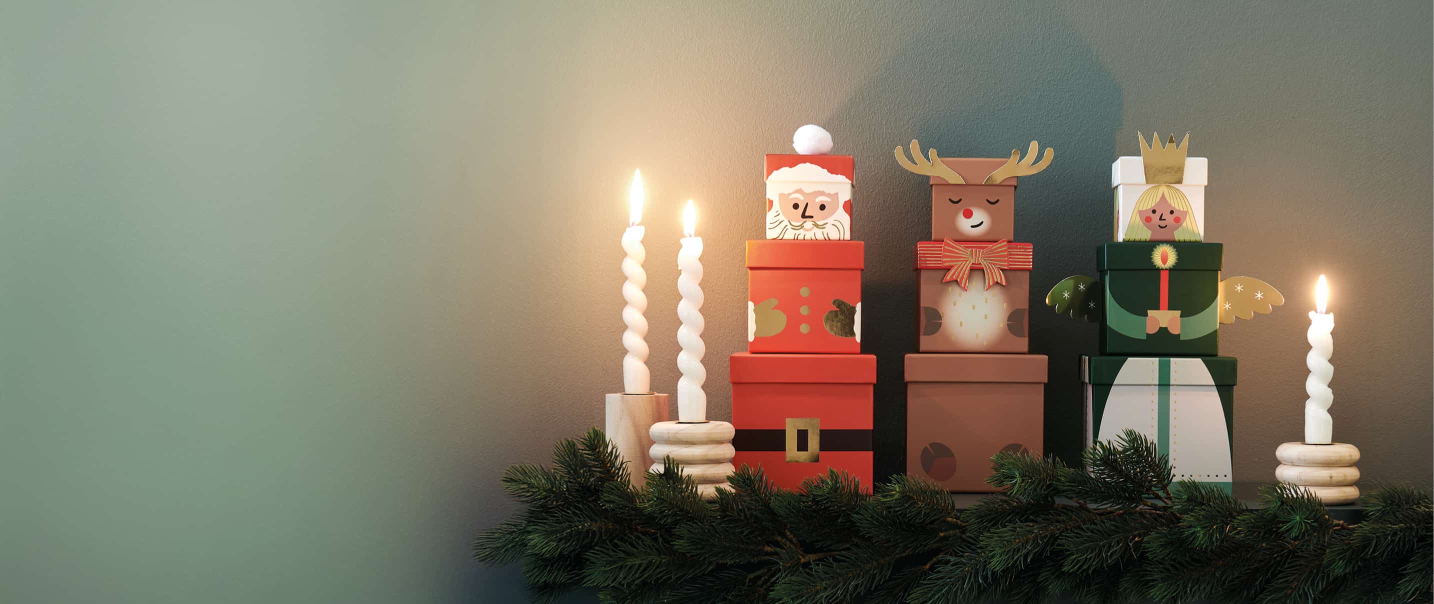 Die Geschenkboxen-Sets mit Weihnachtsmann, Rentier und Engel sind weihnachtlich mit Tannenzweigen und Kerzen dekoriert.