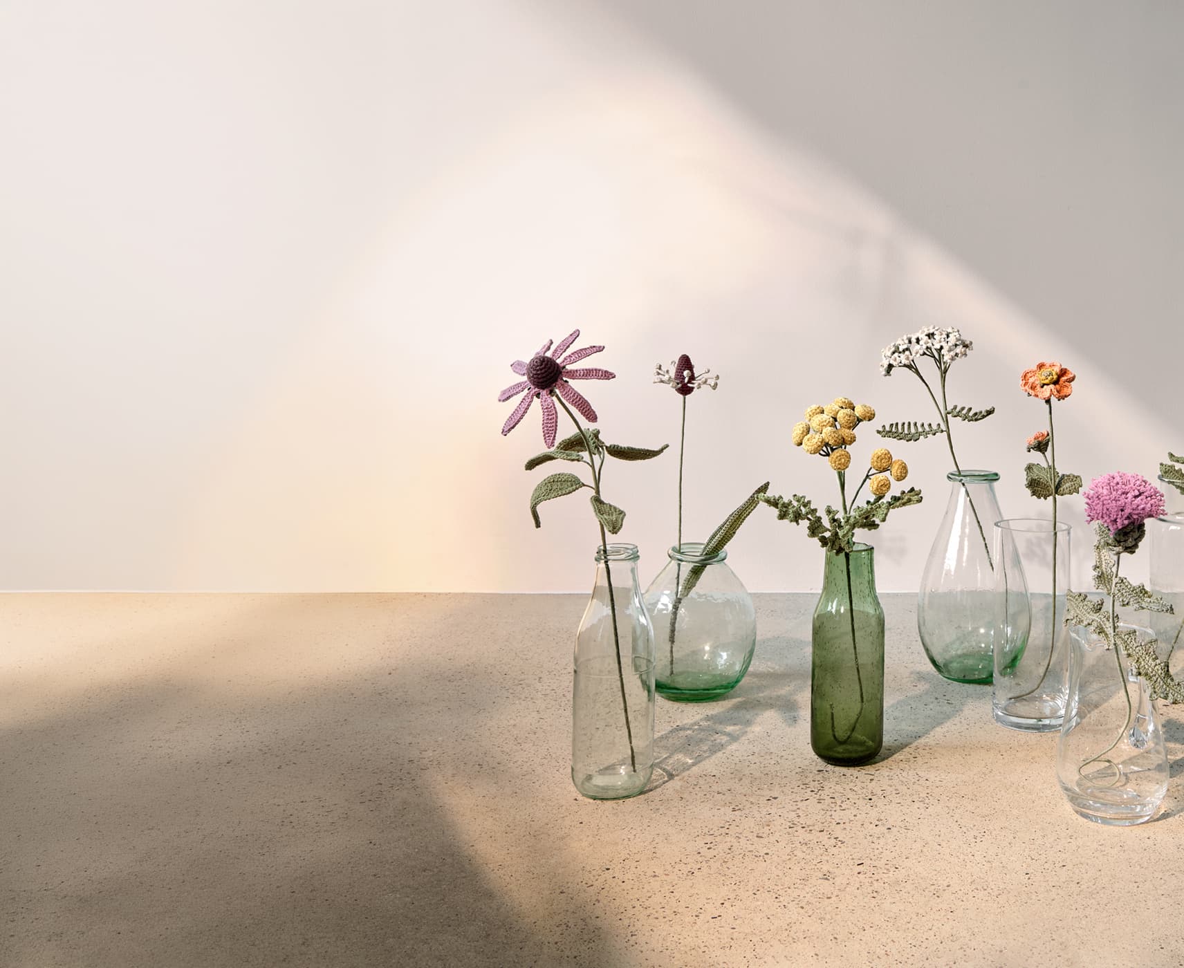Gehäkelte Wiesenblumen stehen dekorativ in Glasvasen. 
