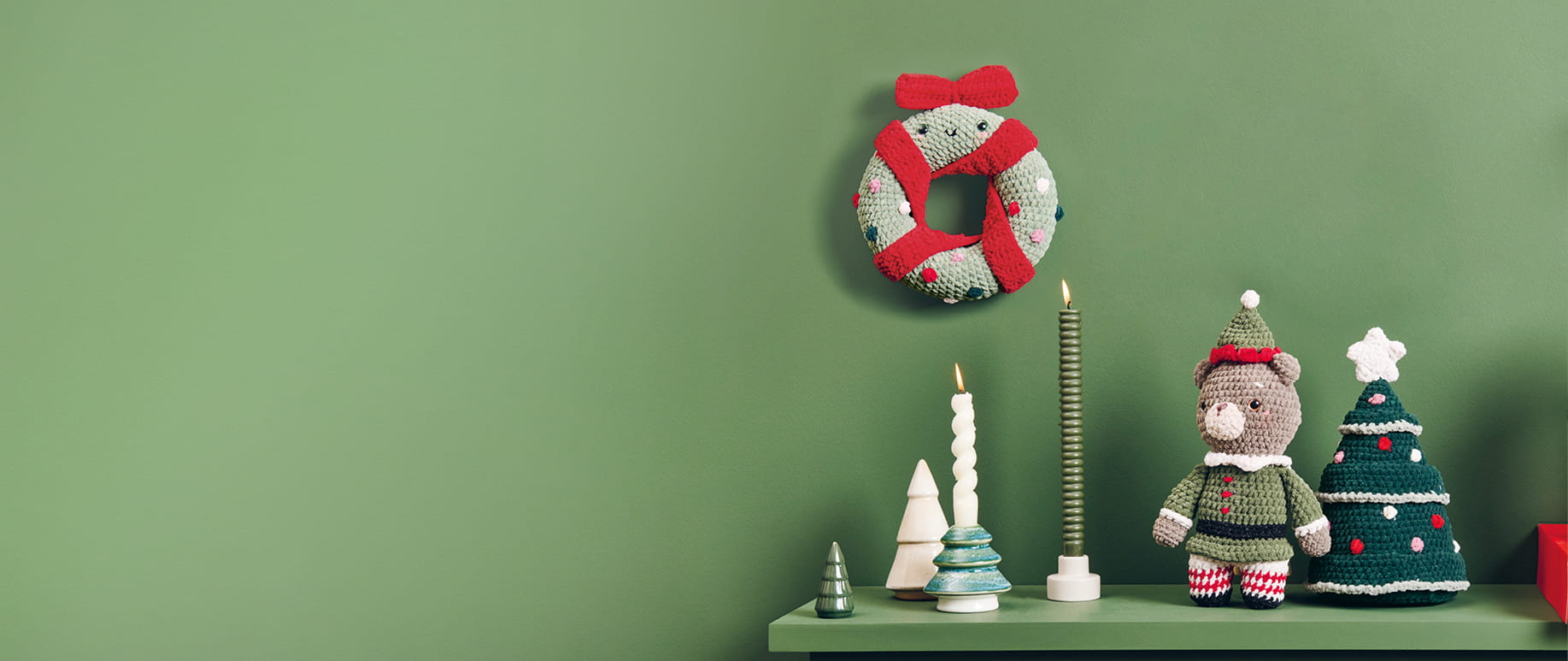 Weihnachtliche Häkelfiguren aus Chenille-Garn sind dekoriert auf einem Regal und an einer grünen Wand dekoriert