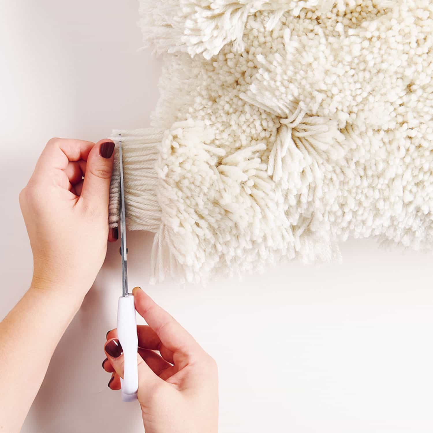 Fäden eines geknüpften Kissens werden mit einer Schere gekürzt