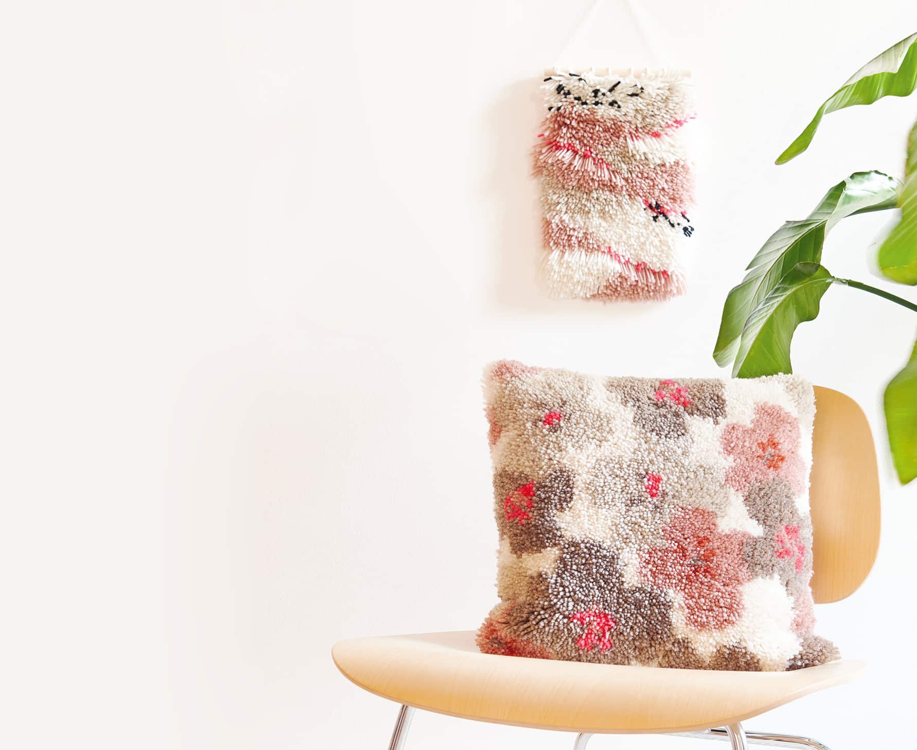 Geknüpfter Wandbehang an weißer Wand und geknüpftes Kissen mit Blumenmuster auf Stuhl