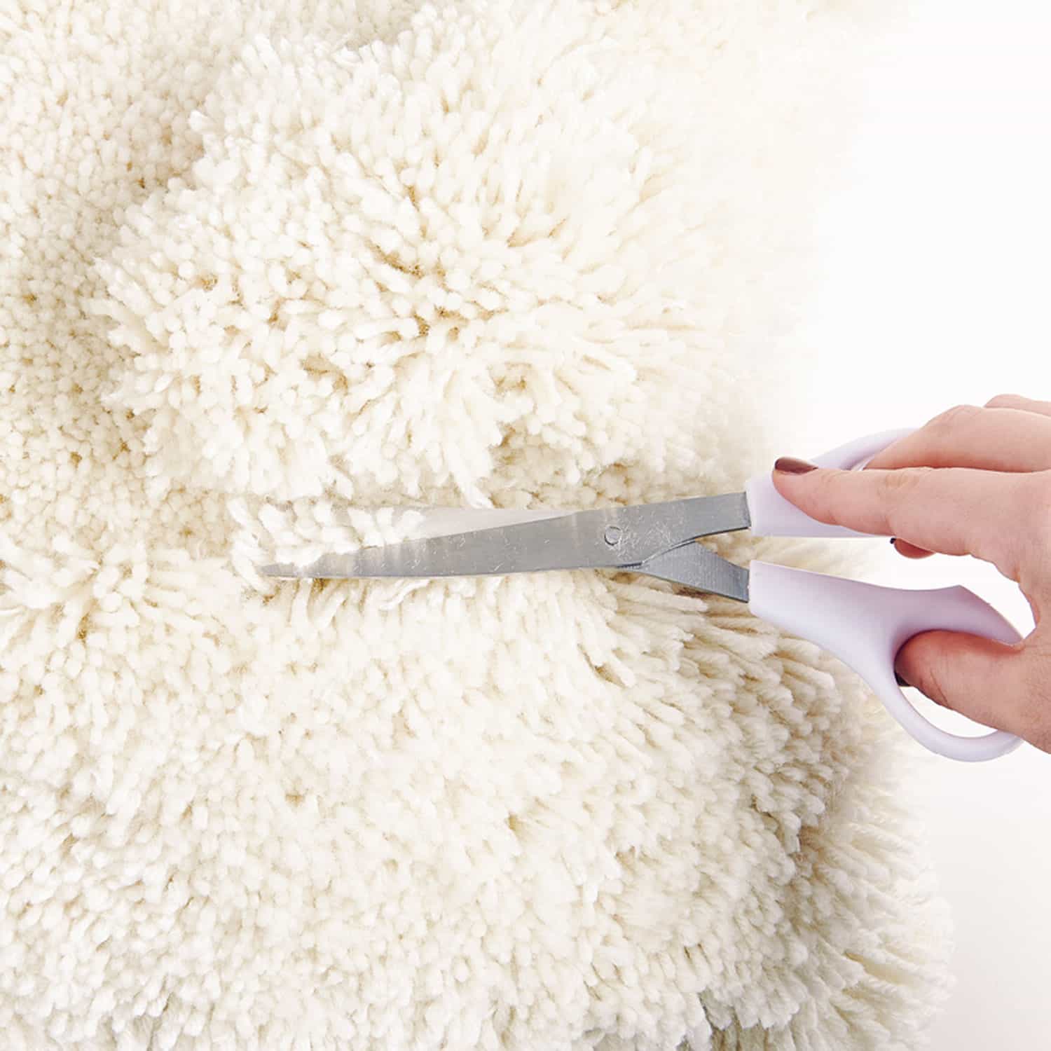 Nahaufnahme eines geknüpften Kissens. Fäden werden mit einer Schere gekürzt