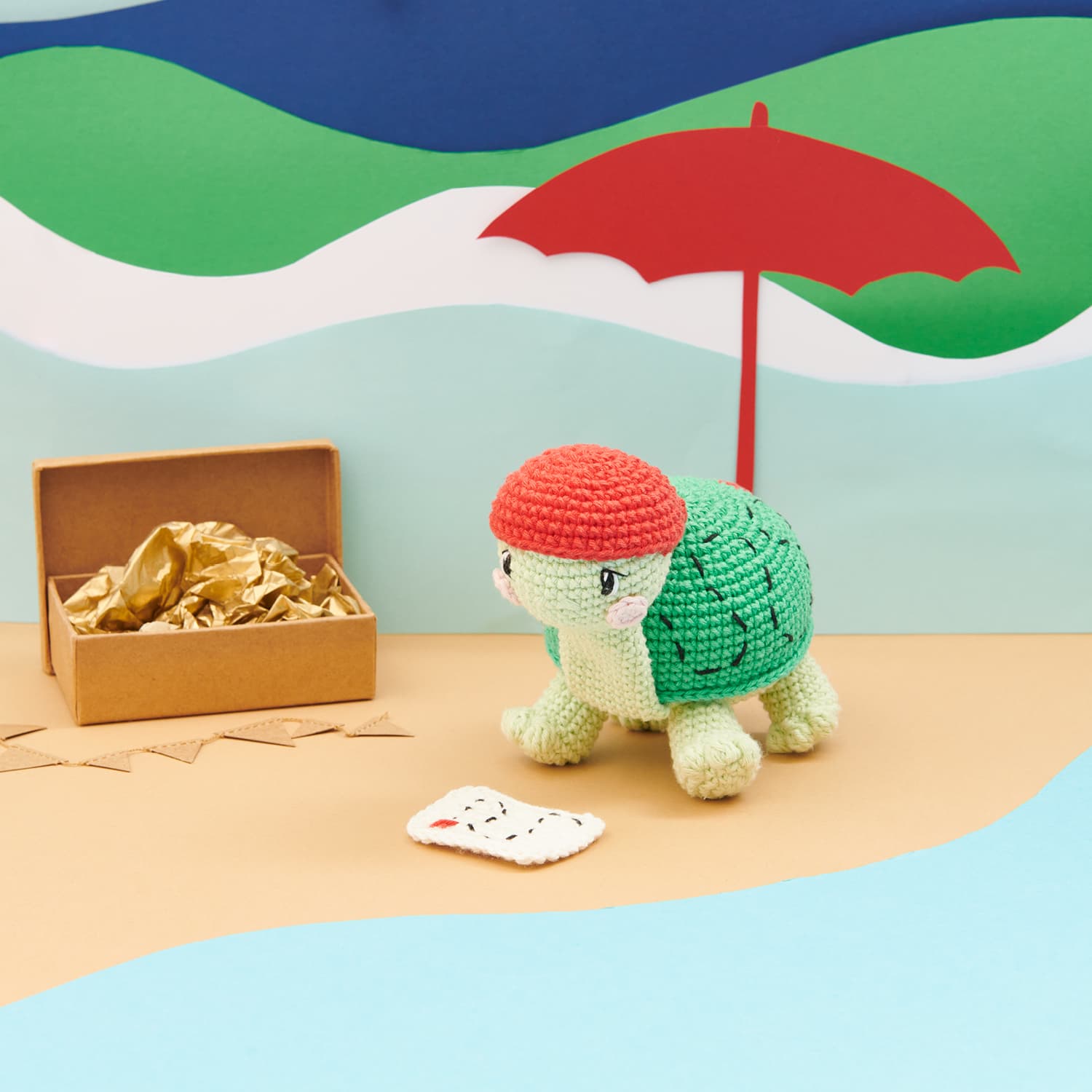 Gehäkelte Schildkröte dekoriert in einer aus Papier gestalteten Strandlandschaft
