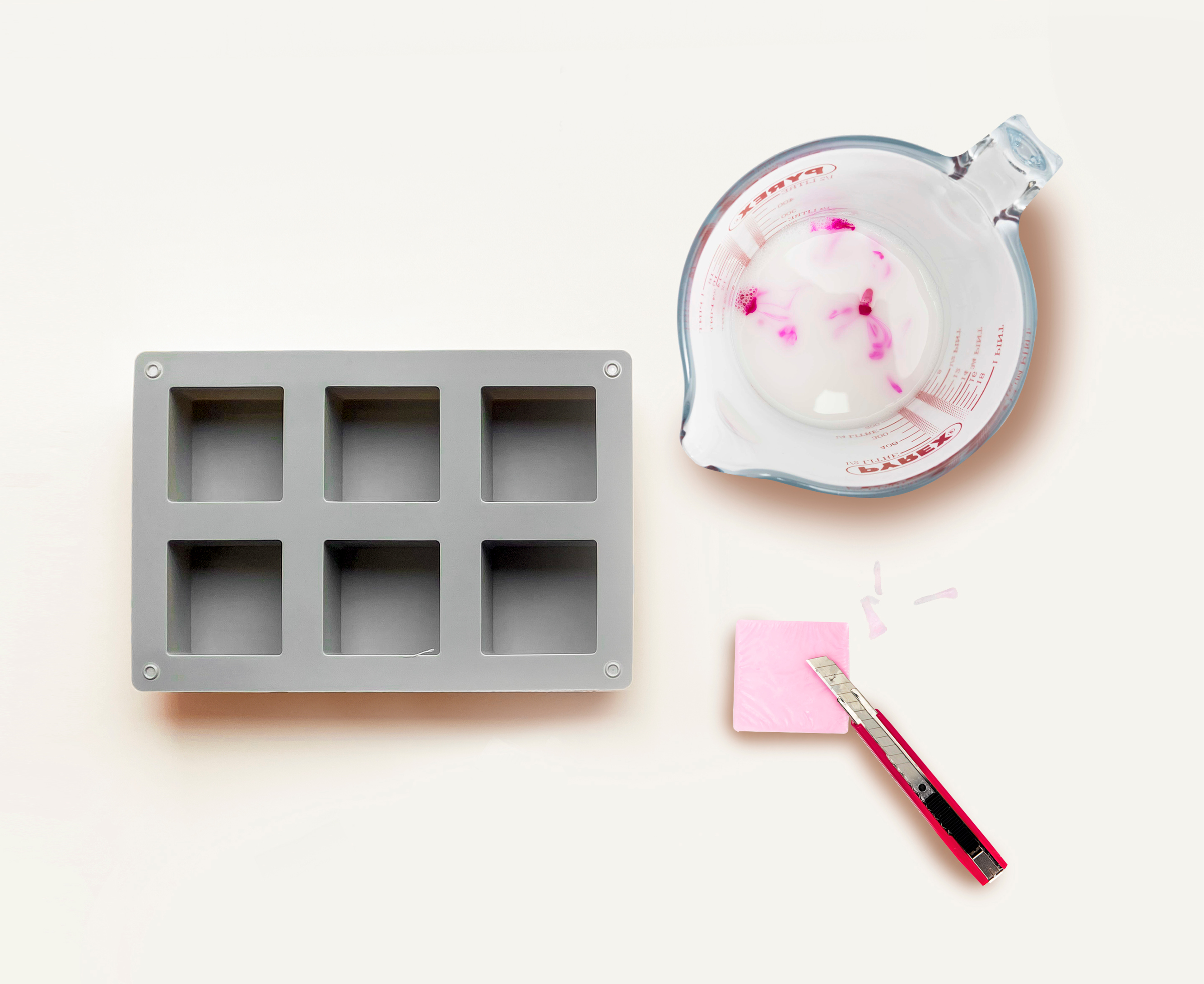 Seifengießform, ein rosa Seifenstück und ein Messbecher mit geschmolzener Seife