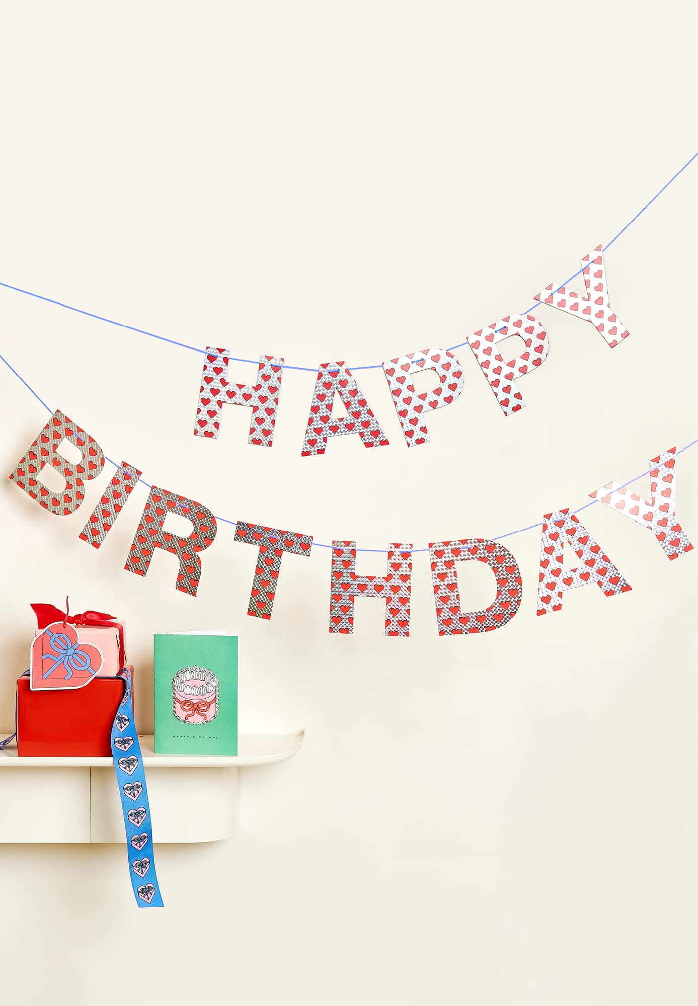 Eine Happy Birthday-Girlande hängt an einer Wand. Davor ist ein Regal mit einem Geschenk und einer Karte.