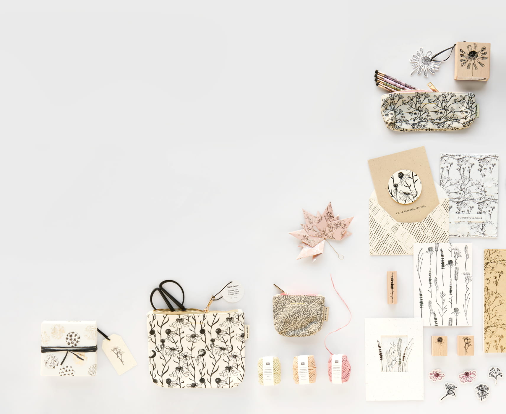 Papeterie- und Geschenkprodukte mit Gräser- und Blumenmotiven in Naturtönen aus der Kollektion "In the Meadow" liegen angeordnet auf grauem Hintergrund.