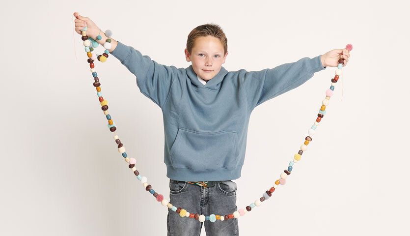 Bastelanleitung Kastanienkette: Kind in blauem Pullover hält lange, bunte Kastanienkette in den Händen.