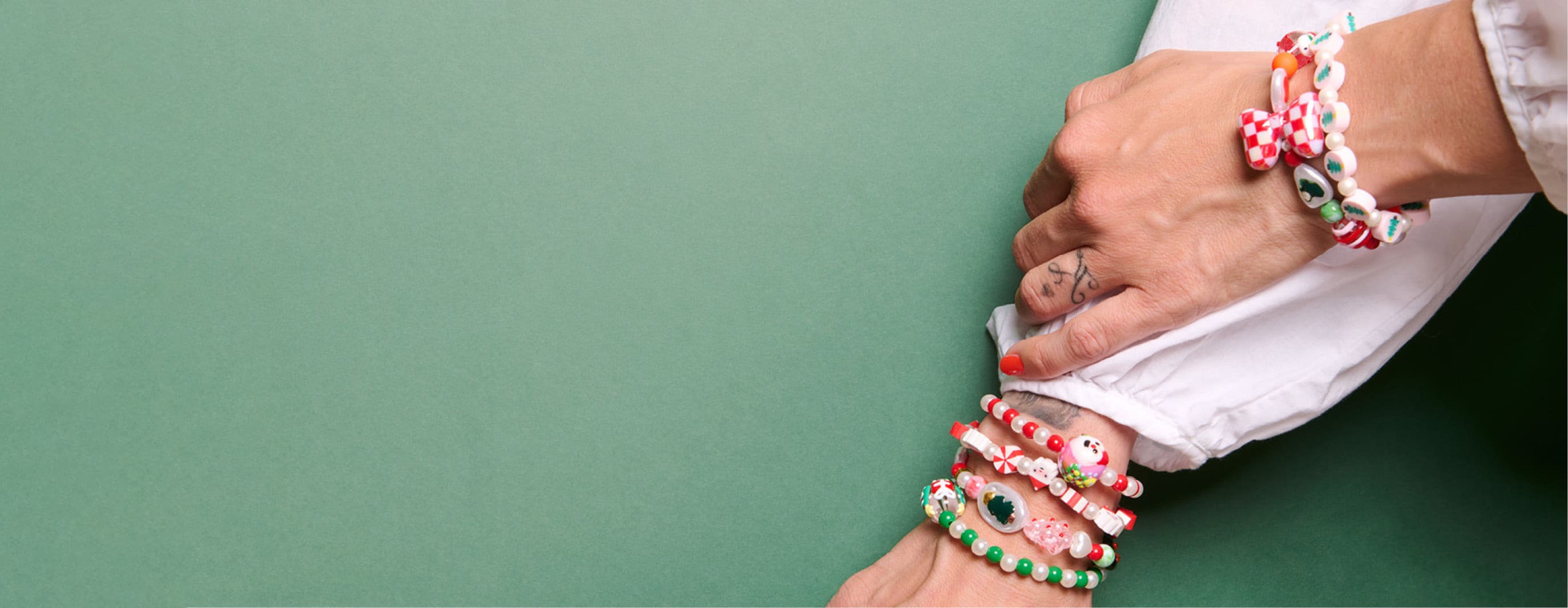 Mehrere selbst gestaltete Perlenarmbänder in weihnachtlichen Farben an den Handgelenken einer Person vor grünem Hintergrund.