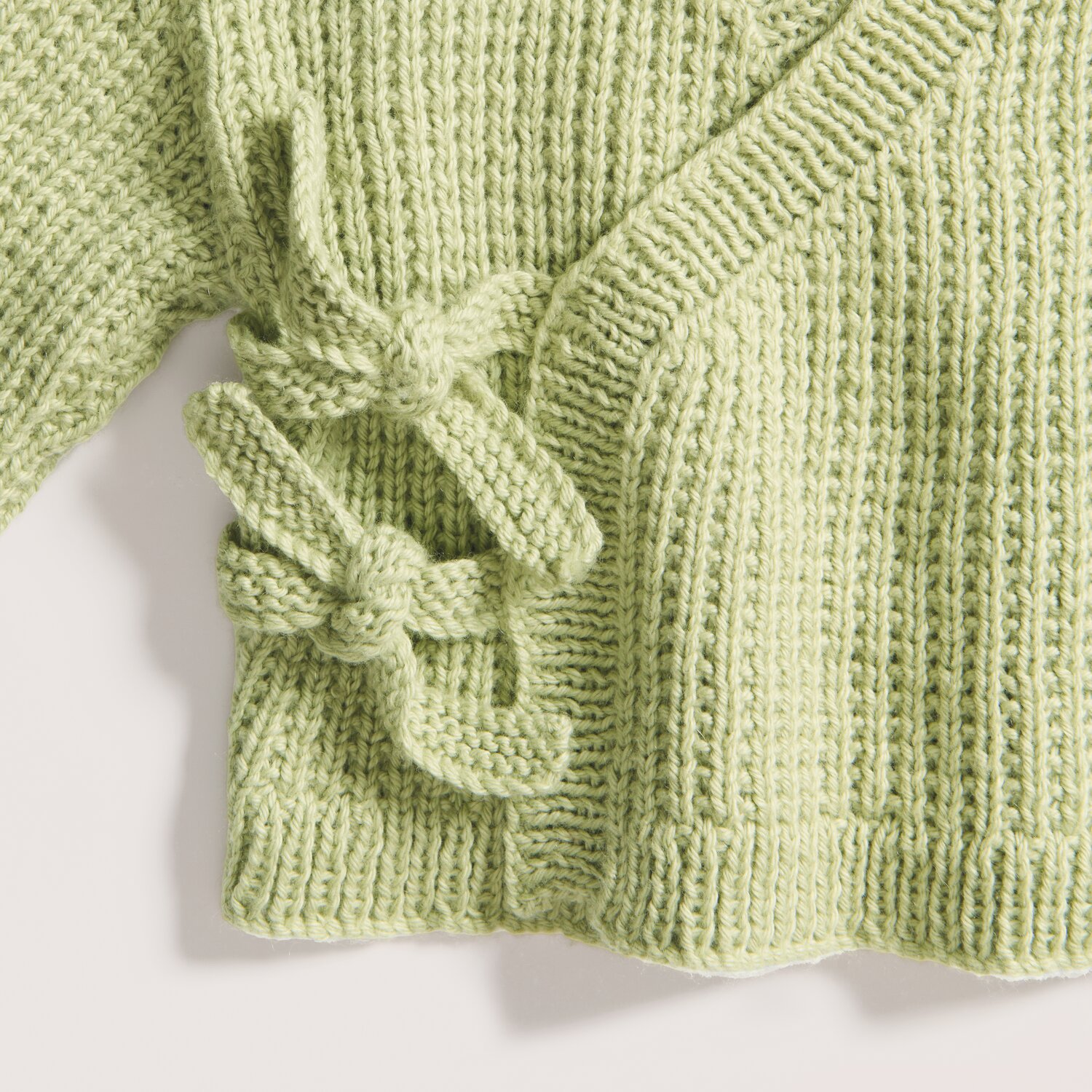 Rico Baby 043 Strickjacke in Salbei mit Schleifen, aus weichem Bio-Baumwoll-Kaschmir-Mix.