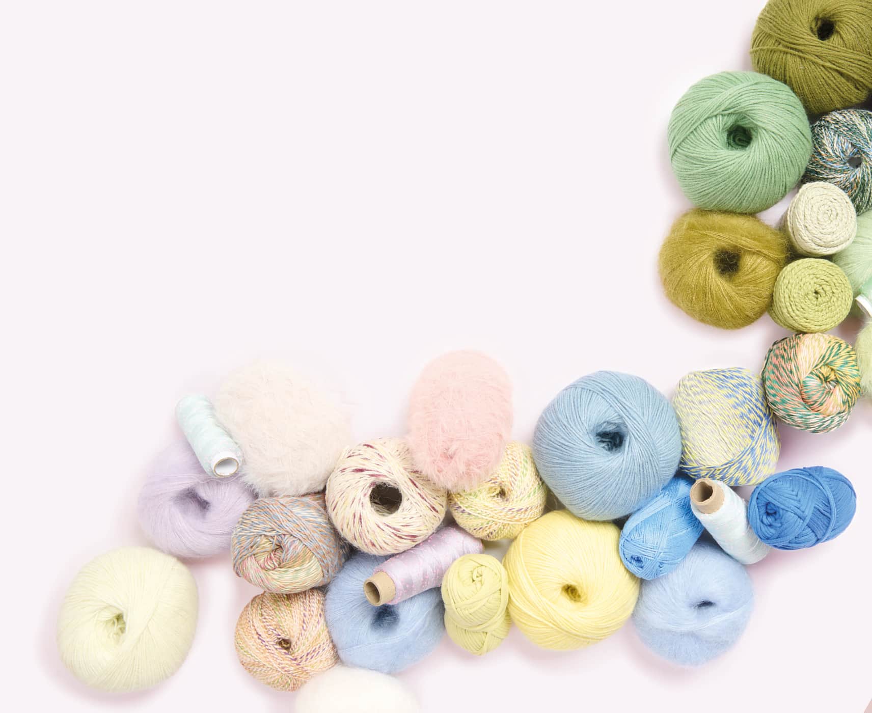Wollknäuel in sommerlichen Farben liegen übereinander gestapelt auf hellem Hintergrund. 