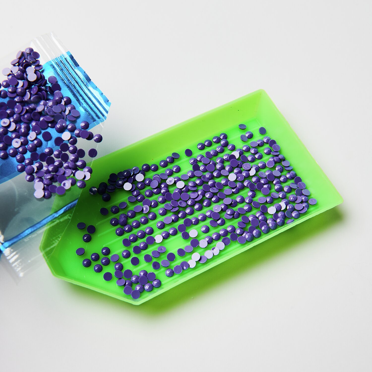 Diamond Painting Aufhänger Tiere, 29-teilig: Lila Strasssteine auf grünem Tablett für kreatives Basteln.