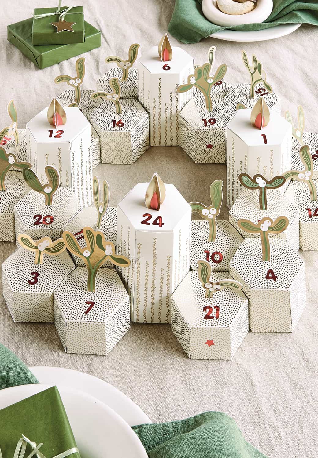 Ein Adventskalender aus Papierschachteln in weiß und Gold steht dekorativ auf einem Tisch.  