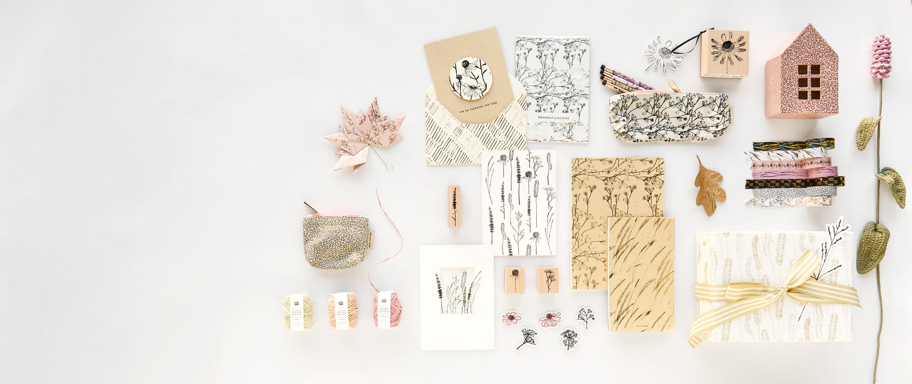 Papeterie- und Geschenkprodukte mit Gräser- und Blumenmotiven in Naturtönen aus der Kollektion "In the Meadow" liegen angeordnet auf grauem Hintergrund.