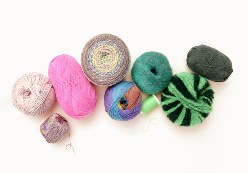 Bunte Wollknäuel liegen nebeneinander drapiert auf hellem Hintergrund