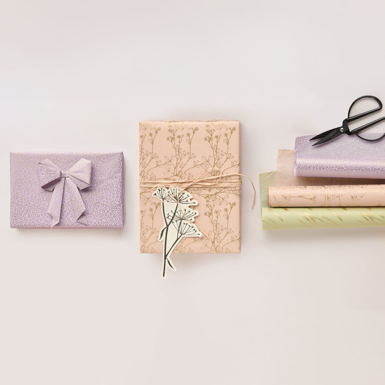 Seidenpapierrollen in Pastelltönen und verpackte Geschenke liegen auf grauem Hintergrund. 