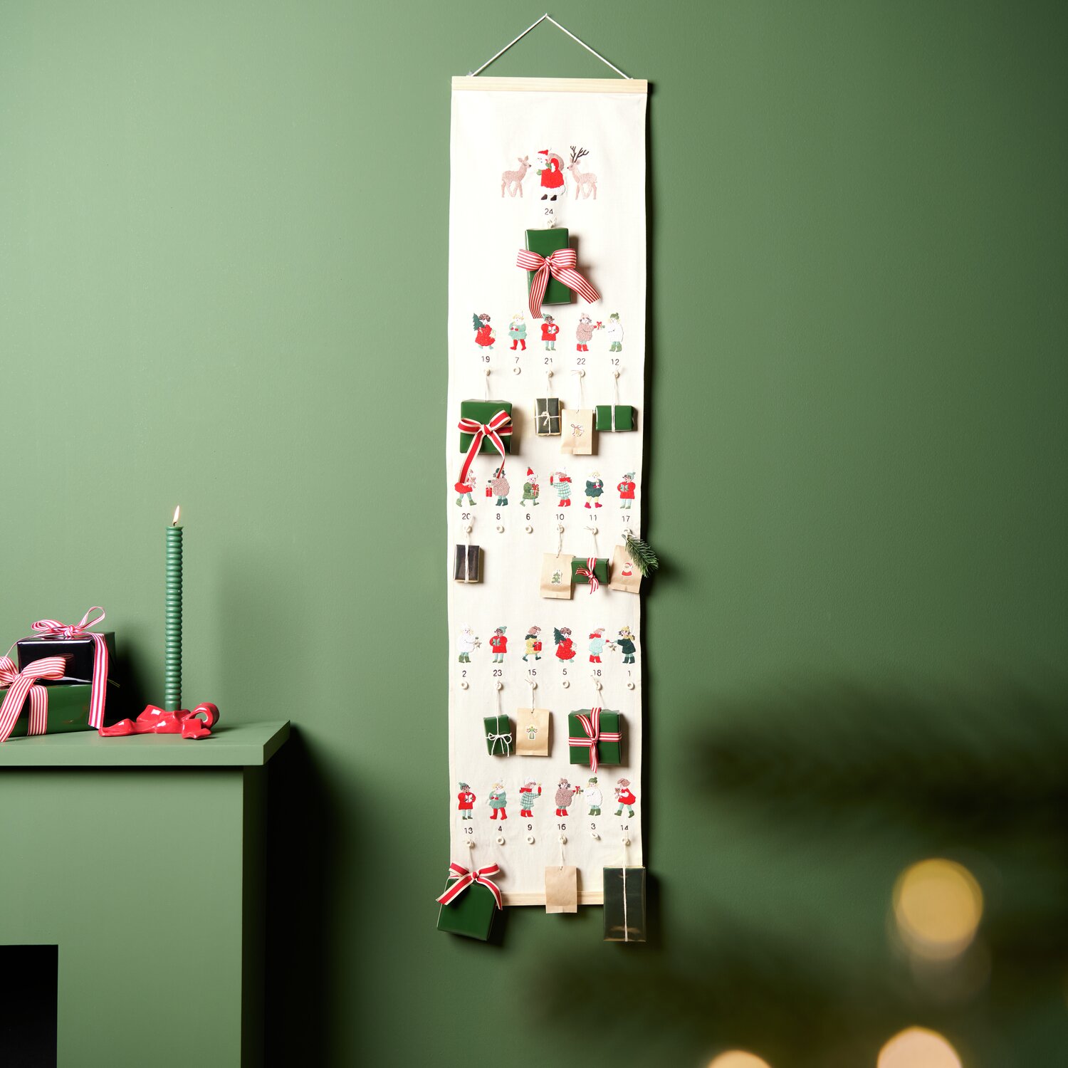 Stickpackung Adventskalender Kinder vorgezeichnet 30x120cm von Rico Design Stickpackung Adventskalender Kinder vorgezeichnet: Ein dekorativer Adventskalender mit kleinen Geschenken und weihnachtlichen Motiven an einer grünen Wand.