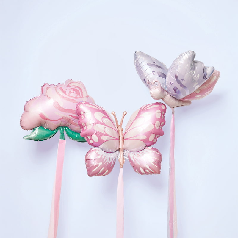 Drei Folienballons in Form von Rose und Schmetterlingen sind mit Kreppbändern geschmückt und stehen vor hellblauem Hintergrund