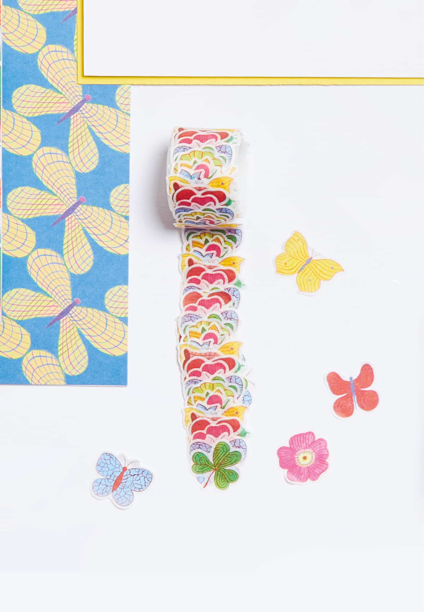 Washi Sticker Rolle mit Blumen, Schmetterlingen und Kleeblettern auf grauem Untergrund ausgelegt