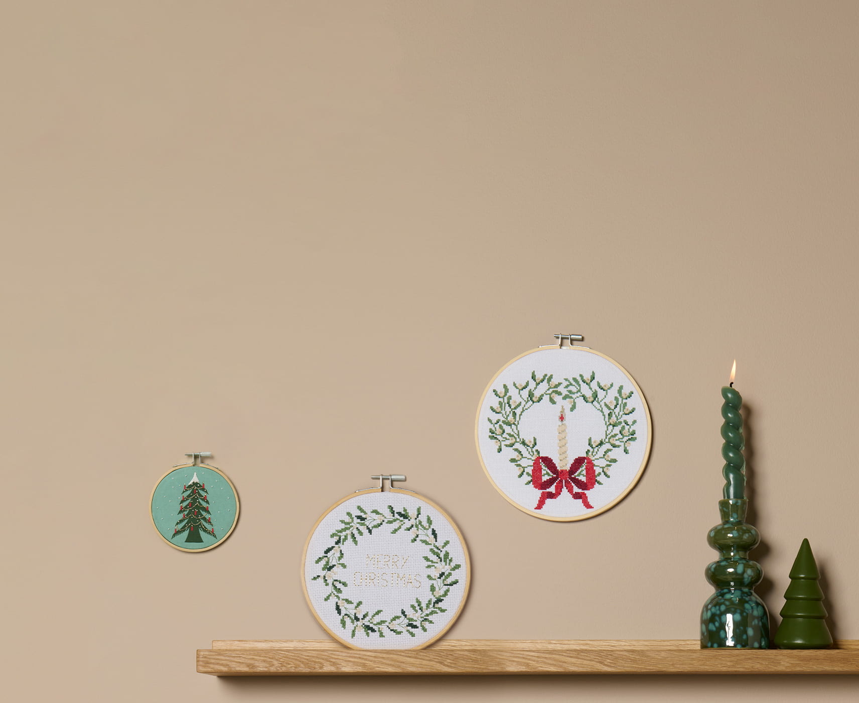 Weihnachtliche Kreuzstichmotive in Stickrahmen mit Tannenbaum, Kerzenkranz und Schriftzug „Merry Christmas“ als Wanddekoration.