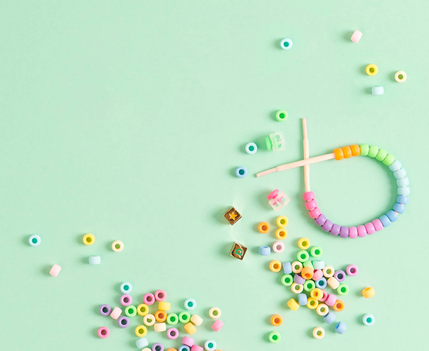 Bunte Itoshii Ponii Beads Großlochperlen liegen verteilt auf grünem Hintergrund. Ein Perlenarmband liegt dazwischen. 