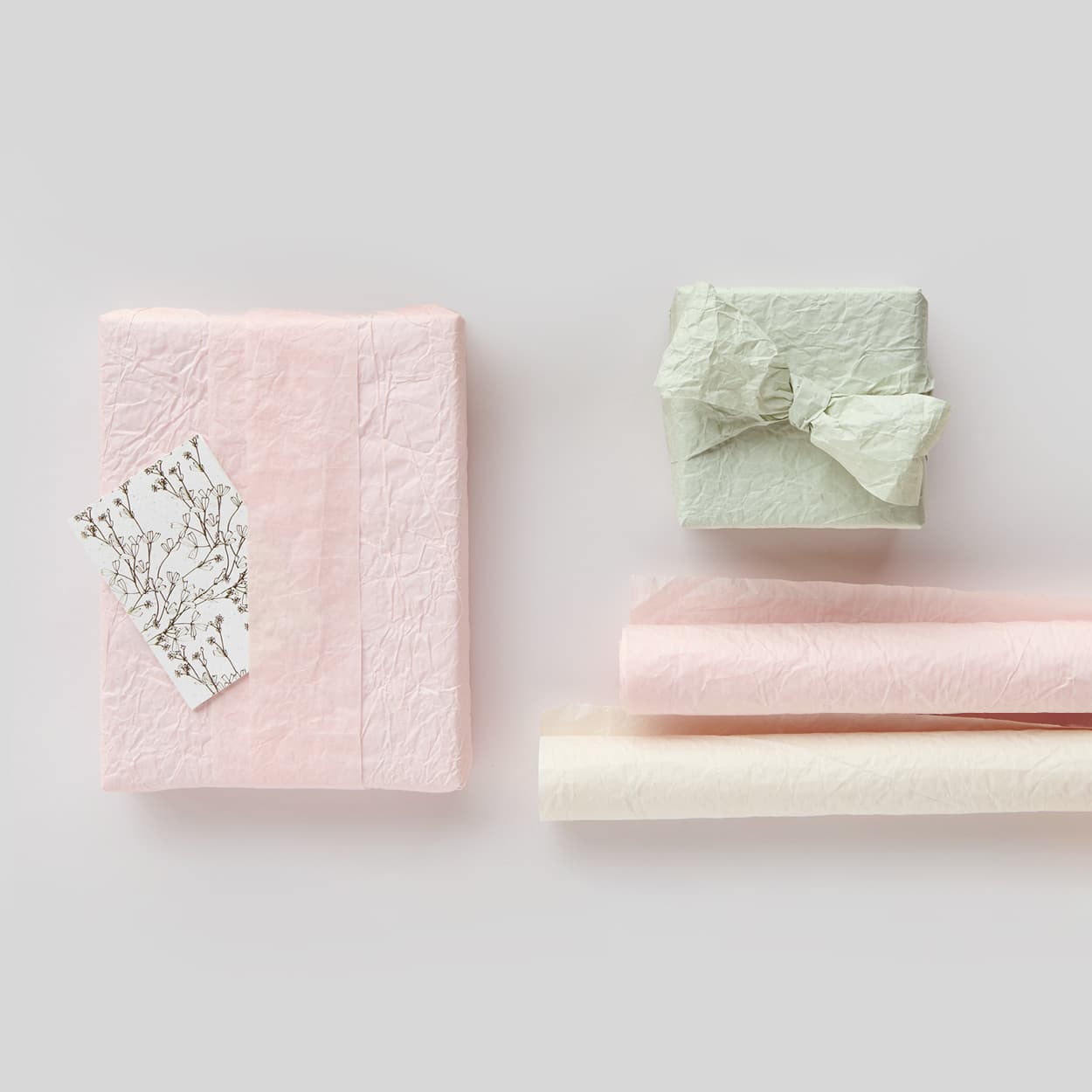 Geschenkpapierrollen und eingepackte Geschenke in Pastelltönen liegen auf grauem Hintergrund.