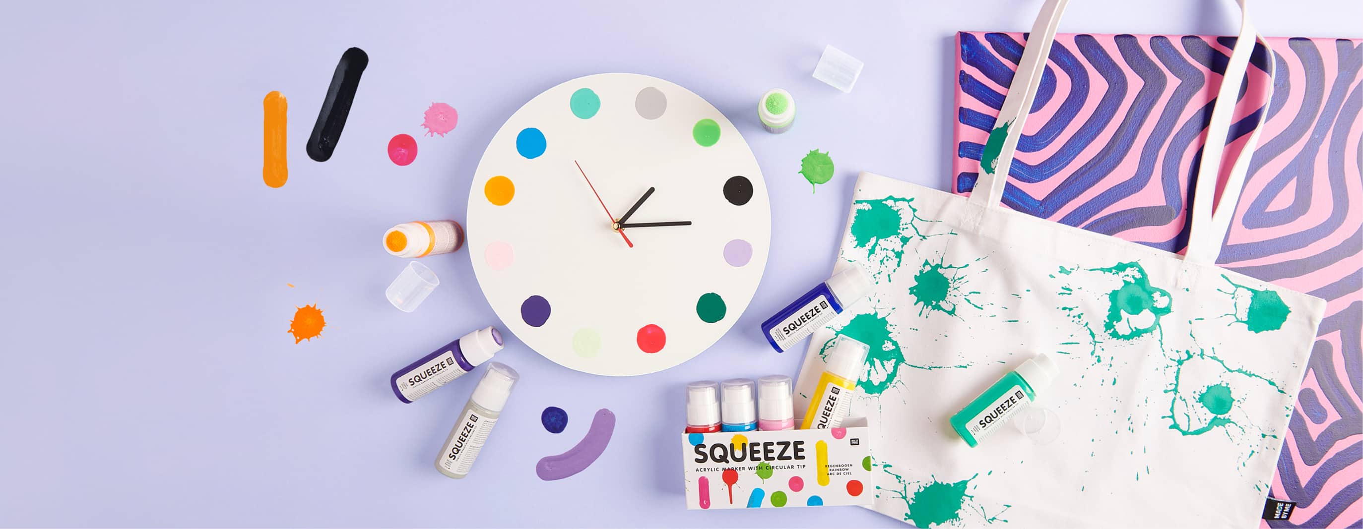 Bemalte Uhr, Tasche und Bild liegen mit Squeeze Markern auf lila Hintergrund ausgelegt
