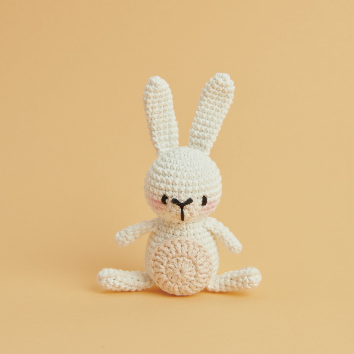 Ricorumi Mini Easy Häkelset - Häschen: Weißes, gehäkeltes Häschen auf orangefarbenem Hintergrund. Ideal für DIY-Projekte.