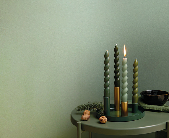 Ein Metalltablett mit Kerzenhaltern ist mit Kerzen in Grüntönen bestückt und weihnachtlich geschmückt.