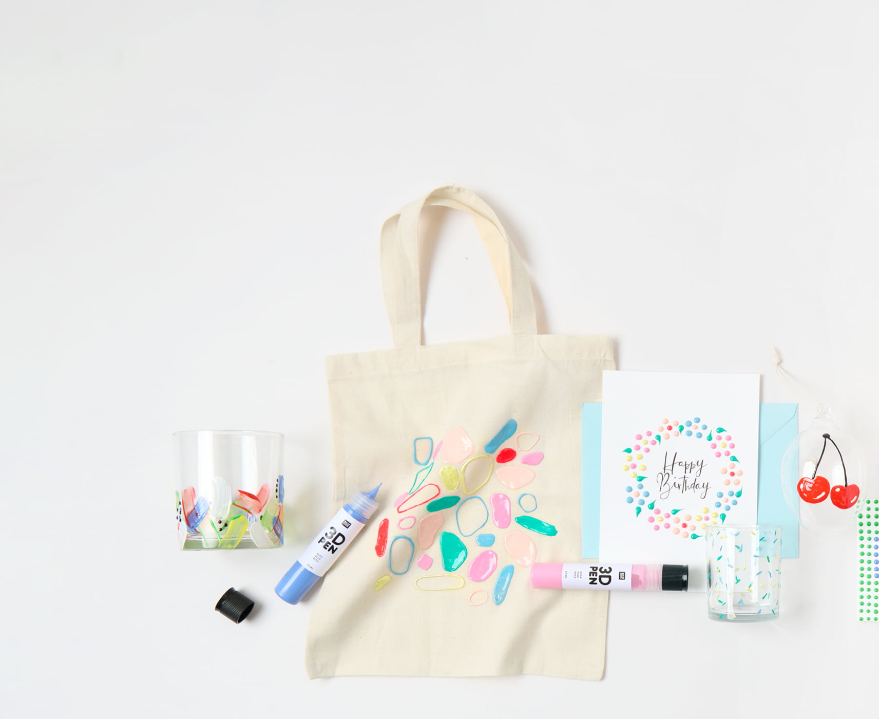 Bunt bemalte Karten, Taschen und Gläser mit 3D- und Perlen-Effekten, liegen umgeben von bunten 3D-Pens auf grauem Hintergrund.