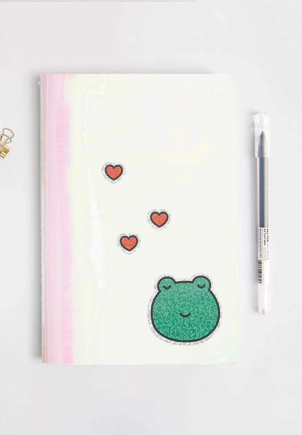 Ein Frosch- und Herz-Sticker kleben dekorativ auf einem Notizheft.