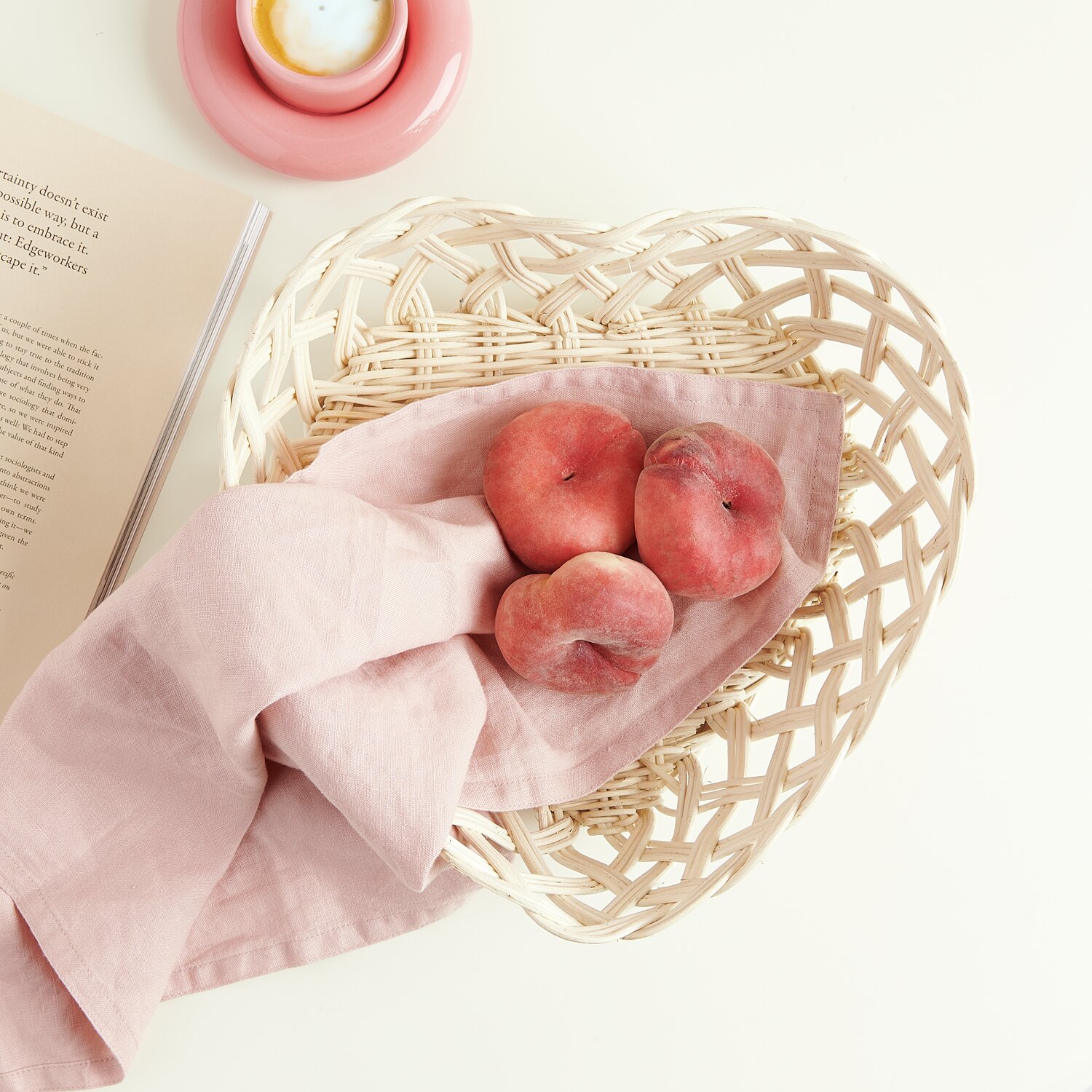 Rattan Korb Herzform Weiß: Ein herzförmiger Rattankorb mit Pfirsichen auf rosa Stoff, ideal für Dekoration.