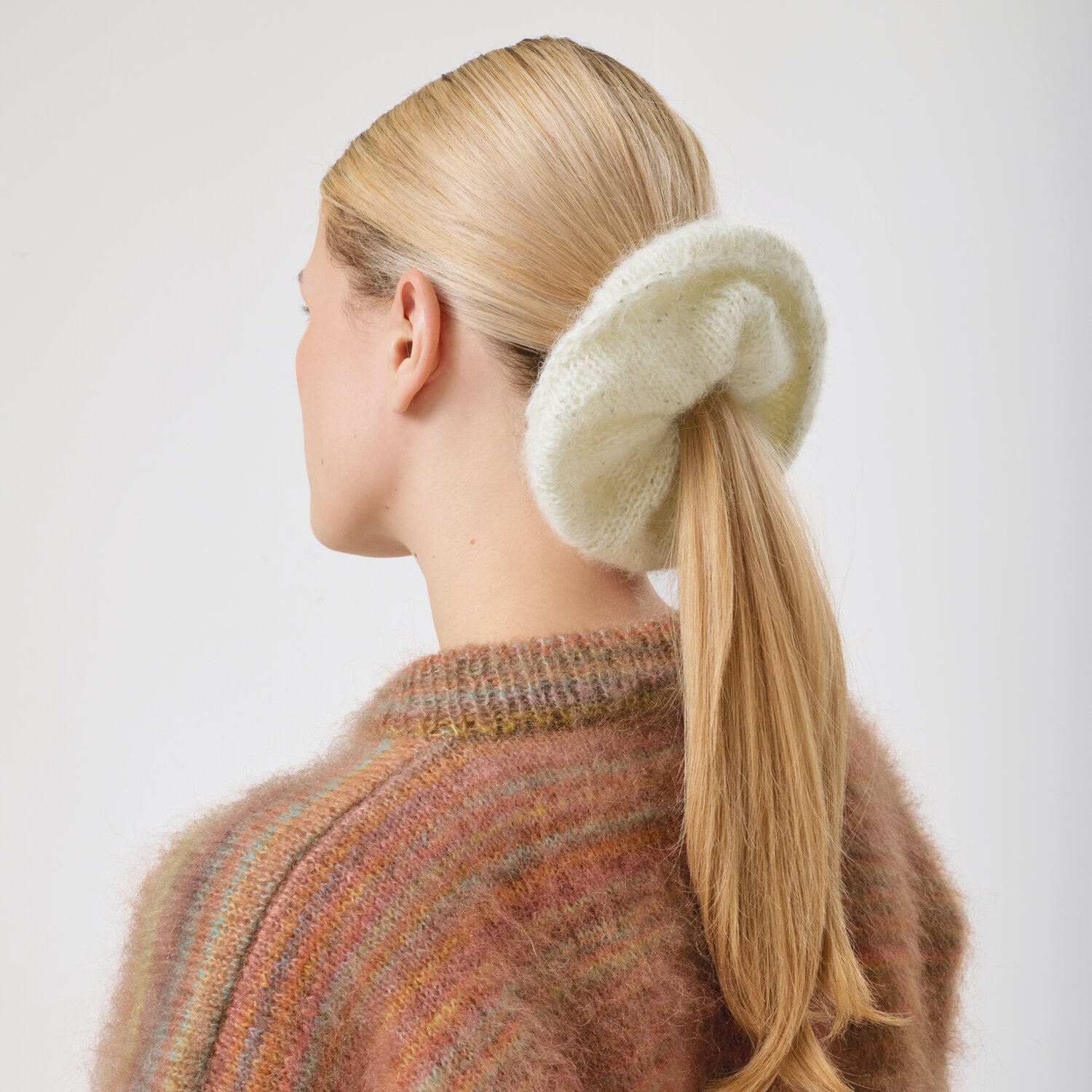 Strickset Scrunchie Modell 18b aus Made by Me No. 21 von Rico Design Strickset Scrunchie Modell 18b aus Made by Me No. 21: Frau mit hellem Scrunchie im Haar, trägt einen bunten Pullover.