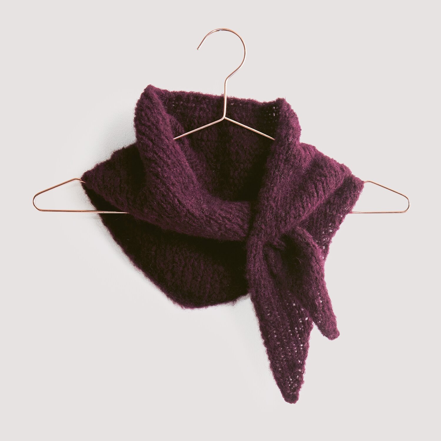 Luxury Knits - Premium Natural Fibres Sprachauswahl deutsch von Rico Design Strickset Dreieckstuch Modell 04 aus Luxury Knits, weinrot, auf Kupferbügel vor grauem Hintergrund.