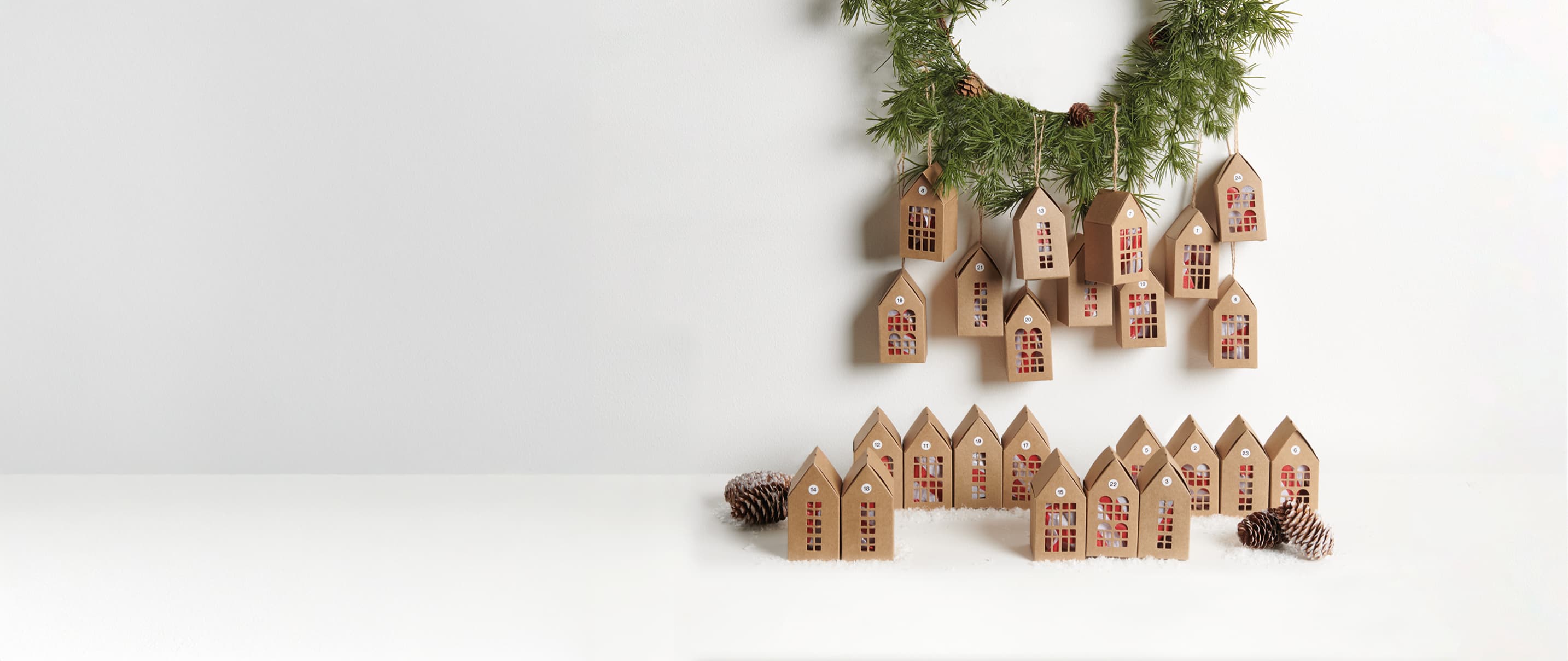 Adventskalender in Form von Papphäusern sind weihnachtlich aufgestellt und an einem Kranz dekoriert