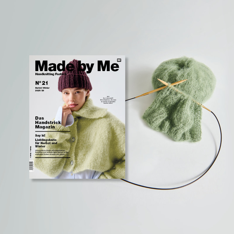 Strickheft Made by Me Nr. 21 neben einem Wollknäuel und Strickstück auf Stricknadeln