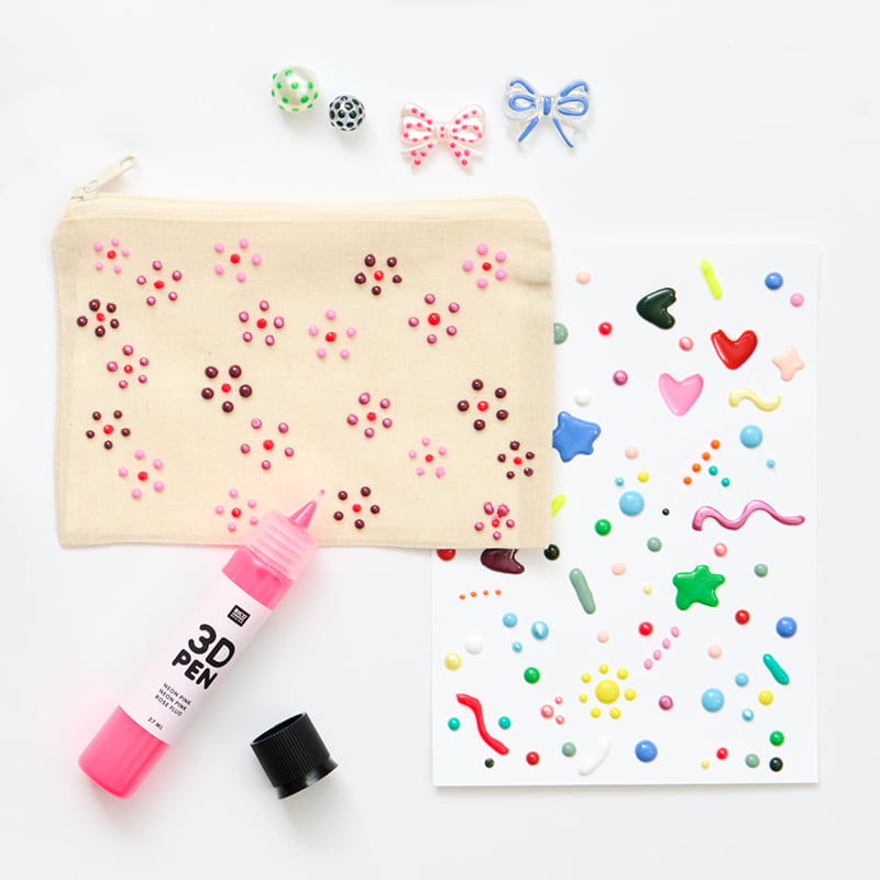 Mit Blumen bemalte Tasche, bunt verzierte Karte und Perlen sind zusammen mit einem 3D Pen in Pink angeordnet.