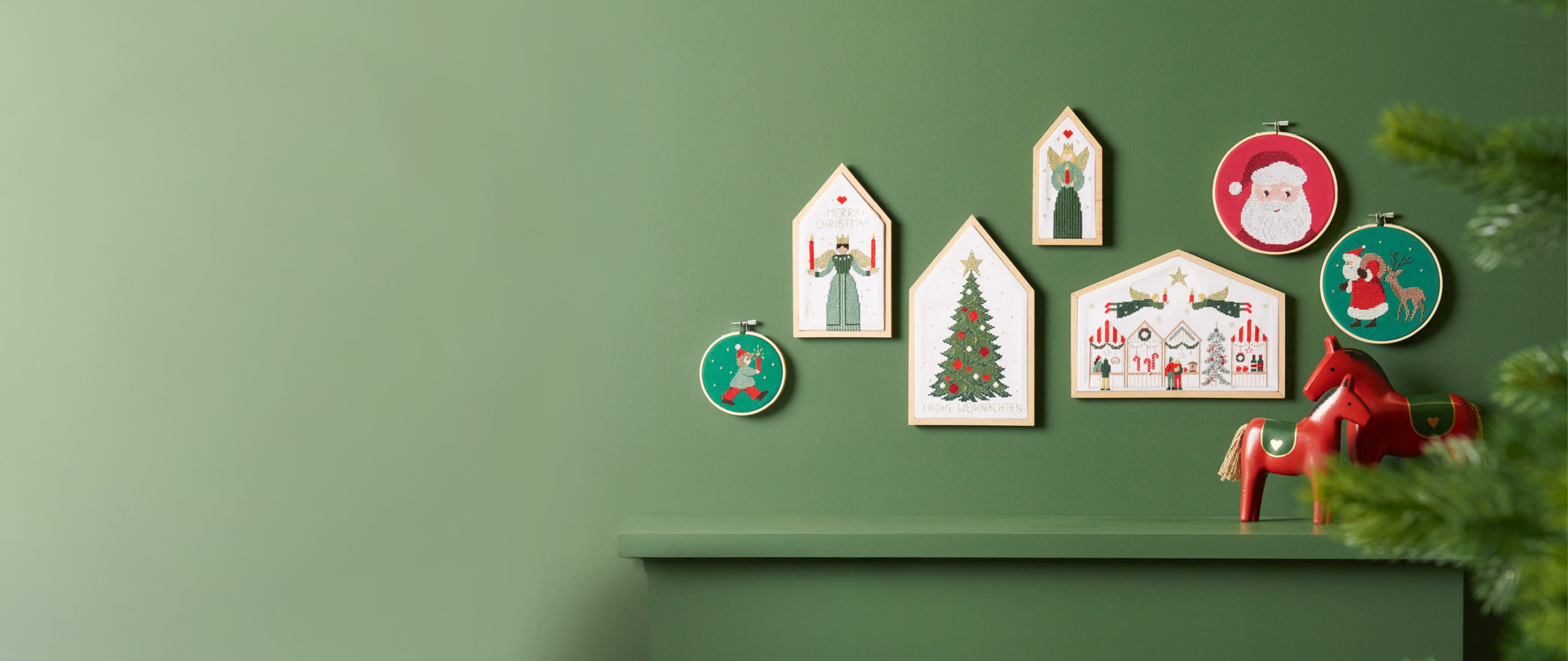 Stickbilder in verschiedenen Größen und mit weihnachtlichen Motiven hängen an einer grünen Wand.
