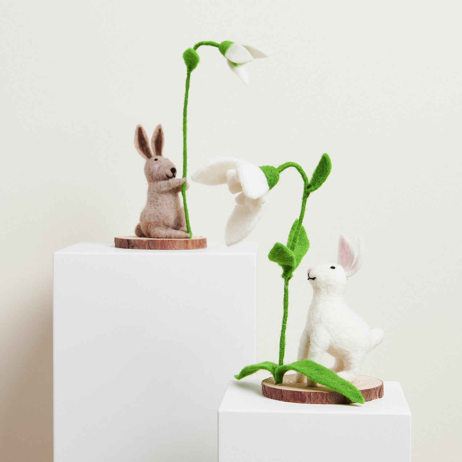Filz-Hase mit Schneeglöckchen: Zwei Hasen aus Filz, einer braun, einer weiß, halten Schneeglöckchen.