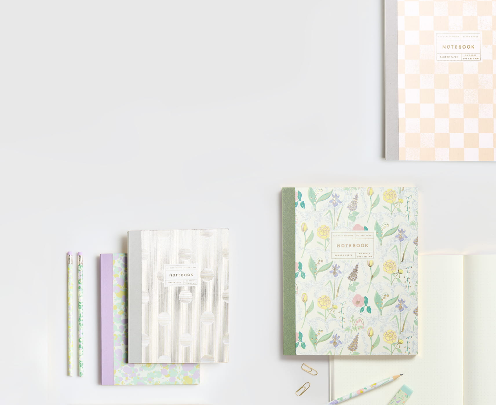 Notizbücher mit floralen und abstrakten Mustern in Pastelltönen liegen auf grauem Hintergrund.