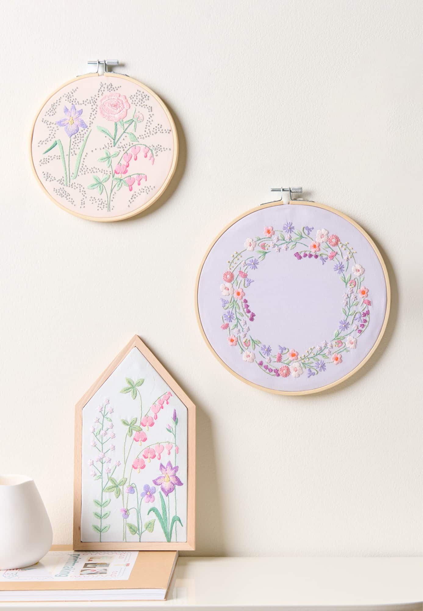Drei Stickbilder mit floralen Motiven sind an einer hellen Wand arrangiert.