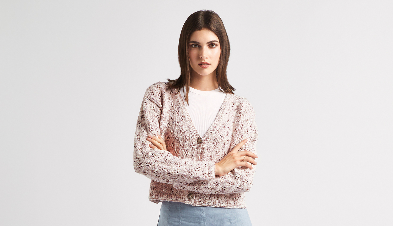 Strickanleitung Lochmusterjacke mit Beilaufgarn: Frau trägt rosa Lochmusterjacke über weißem Shirt, kombiniert mit blauer Jeans.