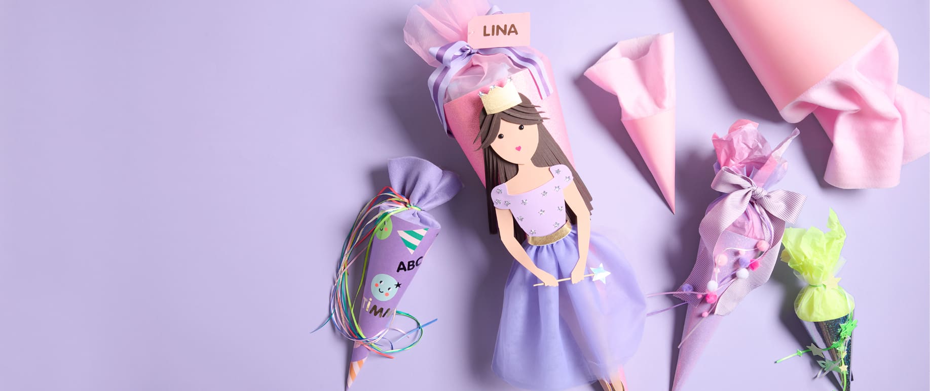 Schultüte mit Prinzessin-Design liegt neben dekorierten Schultüten in kleineren Formaten auf lila Hintergrund
