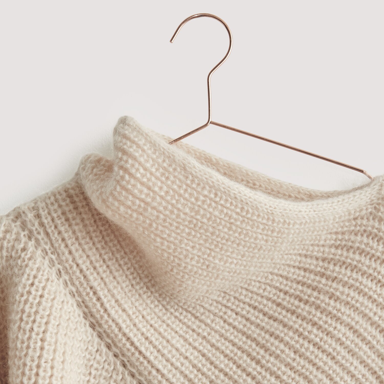 Luxury Knits - Premium Natural Fibres Sprachauswahl deutsch von Rico Design Luxury Merino Alpaca Dream aran: Cremefarbener Strickpullover aus natürlichen Fasern auf Kupferbügel.