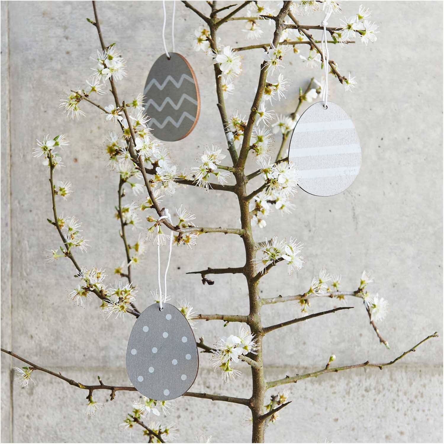 Holzhänger Osterei 3 Stück: Drei silberne Ostereier von Rico Design hängen an blühenden Zweigen.