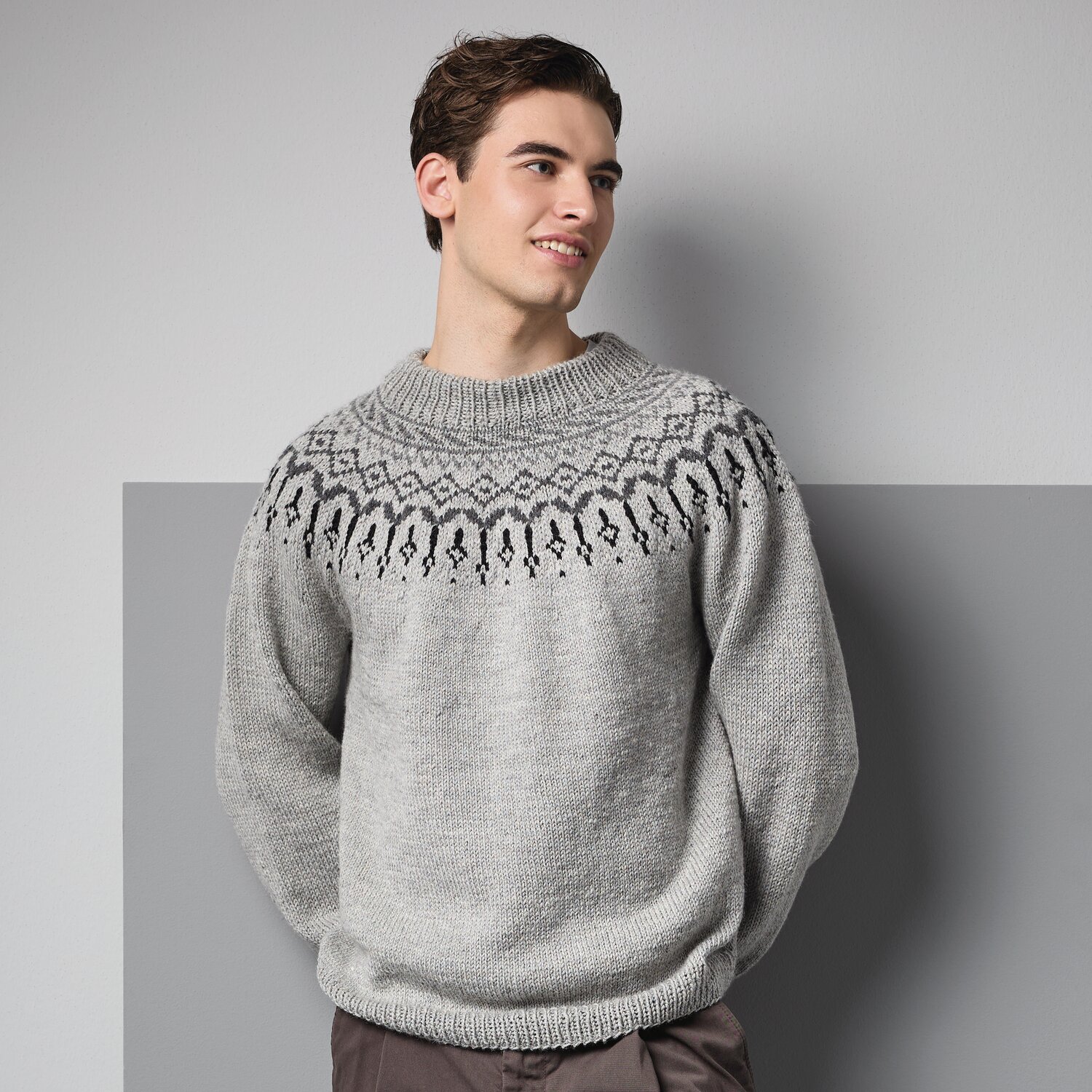 Strickset Pullover Modell 04 aus Made by Me Men No. 3 von Rico Design Strickset Pullover Modell 04 aus Made by Me Men No. 3: Grauer Pullover mit nordischem Muster, getragen von einem Mann vor grauem Hintergrund.
