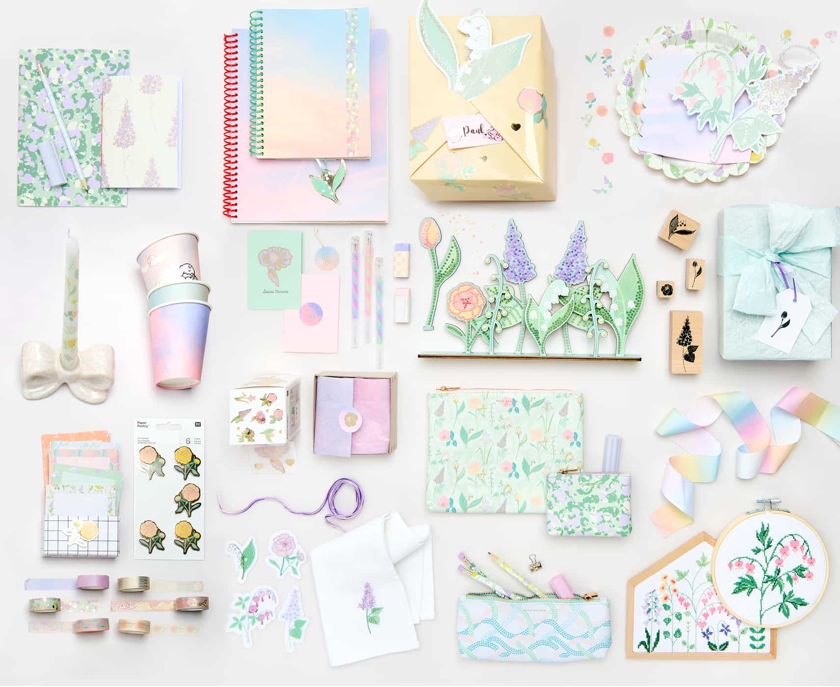 Papeterie-, Partyartikel, Stickbilder und Dekorationen mit Himmel- und Blumendesigns liegen angeordnet auf grauem Hintergrund. 