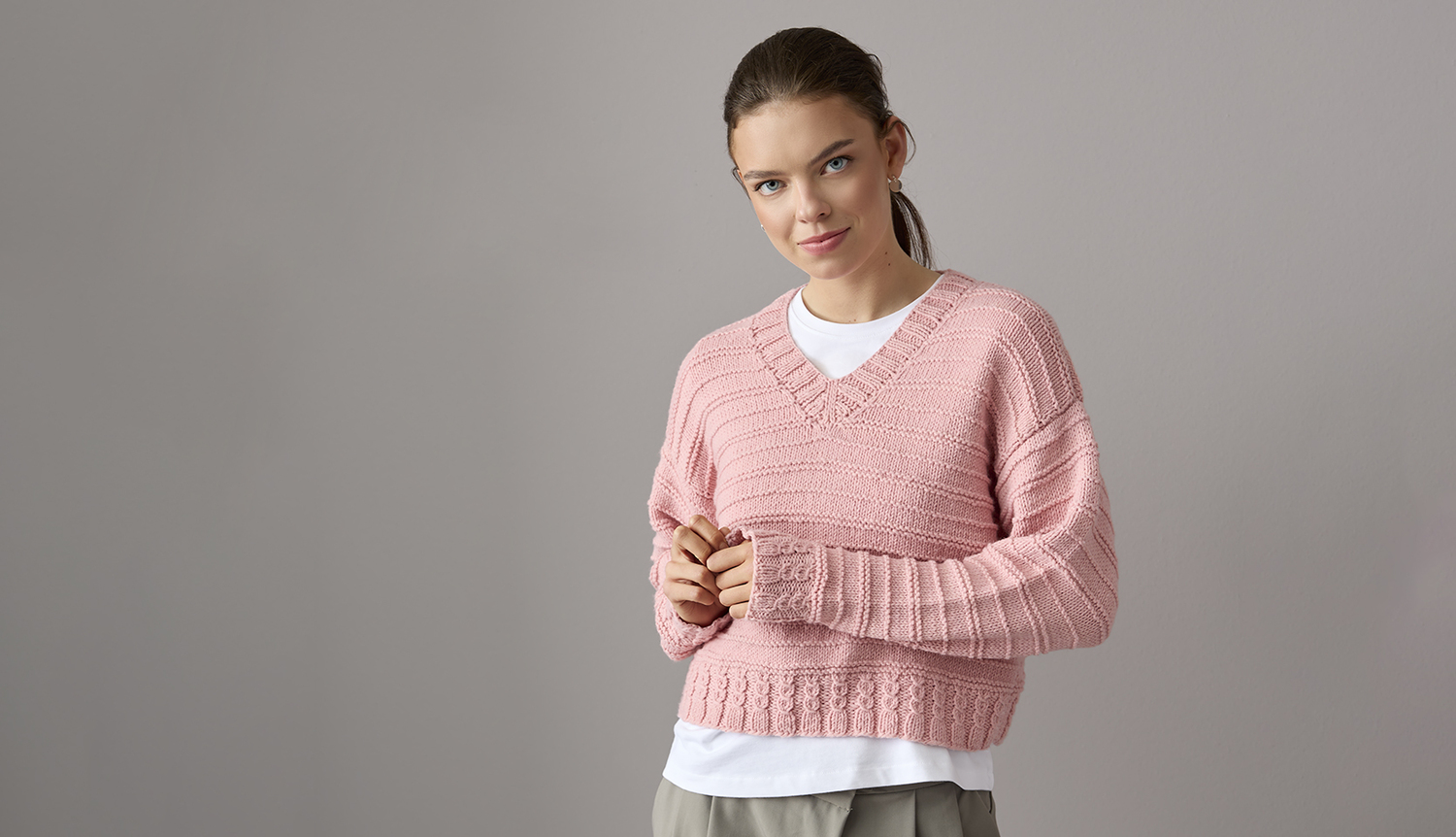 Strickanleitung Pullover aus Essentials Vegan Cashmere aran: Frau trägt rosa V-Pullover.