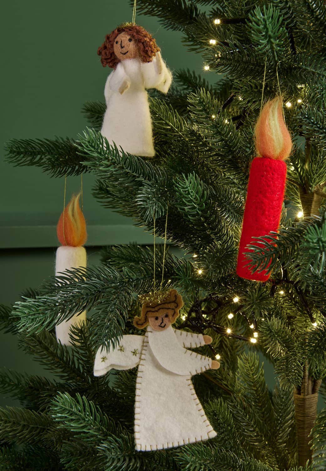 Filzanhänger in Form von Engeln und Kerzen hängen dekorativ in einem Tannenbaum.